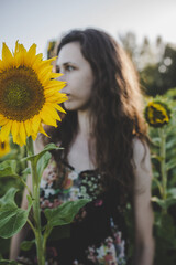 Portrait of a young, attractive, caucasian white woman with brown curly hair on a sunny summer day in countryside, surrounded by yellow, sunflower field