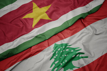 waving colorful flag of lebanon and national flag of suriname.