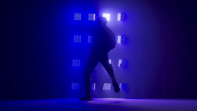 Silhouette of a talented young hip hop dancer. Hip hop street dance on a stage in dark studio with smoke and neon lighting. Dynamic lighting effects. Creative skills. Slow motion.