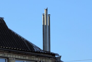 three long gray chimneys on the slate roof of a rural brick house against a blue sky