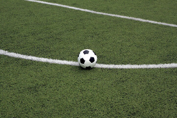 White and black ball for playing soccer lays on green synthetic grass near center of sport playground