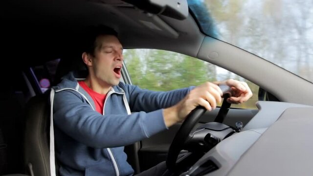 Sleepy driver yawns and closes eyes while driving in car. Yawning and fatigue are danger from traffic accident