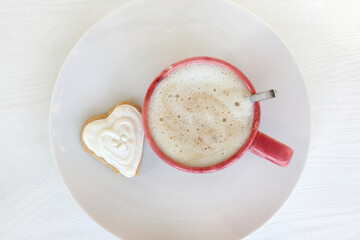 cup with frothy cappuccino and heart-shaped cookies on a plate top view. sweet valentine and...