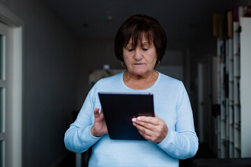 Senior woman standing holding a digital tablet and making a video conference