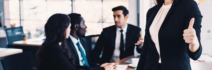 Portrait of business woman leader with busy team behind her, thumbs up. Banner frame.