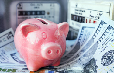 Pink piggy bank and US dollars near an electricity meter and gas meter. Utility bills, consumption...