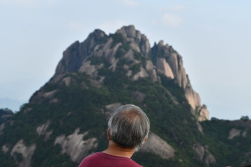 Fototapeta na wymiar Old chinese man from the back is ovserving monumental pick of Huangshan, China