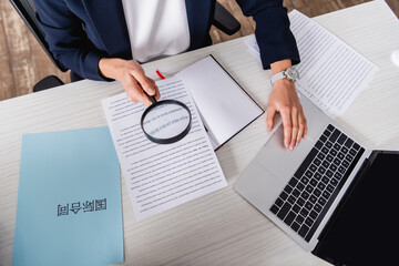 partial view of interpreter holding magnifier near paper with english text and laptop