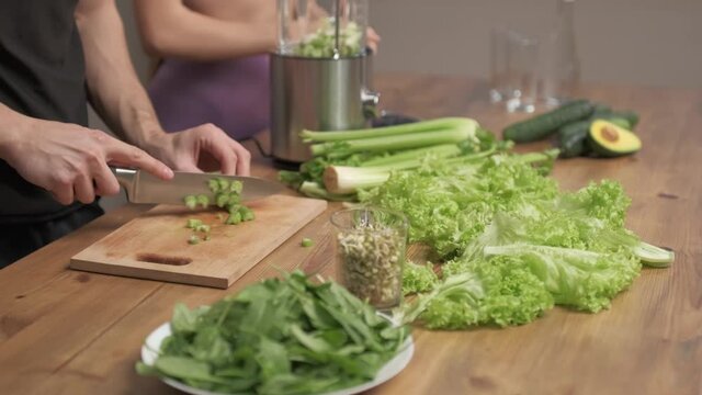 Man cuts the ingredients for making green vegetable smoothies. Woman halpes him. healthy food concept