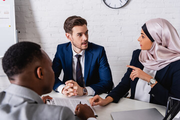 arabian businesswoman in hijab pointing with finger while talking to multiethnic business partners