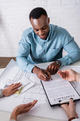 african american businessman signing contract while businesswoman giving him money in envelope,...