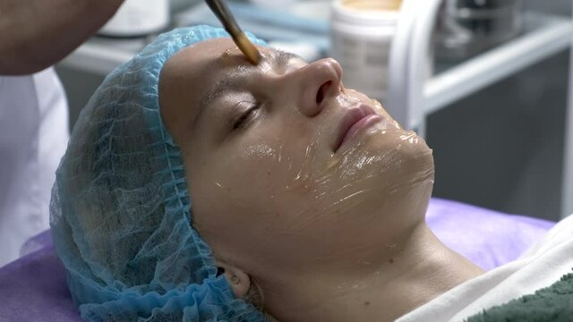 Applying a transparent gel with a brush on the face of the young woman. Cosmetology procedures.