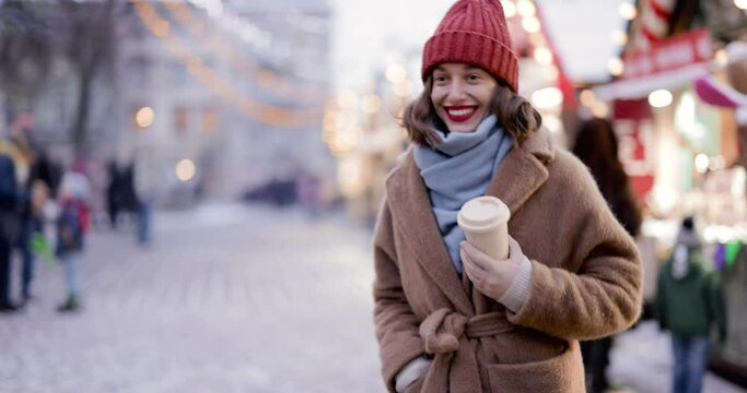Woman enjoying winter holidays at Christmas market, walking with a cup of coffee in the evening in a New Year's decorated city. Handheld video shot