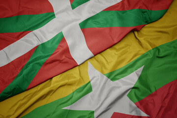 waving colorful flag of myanmar and national flag of basque country.