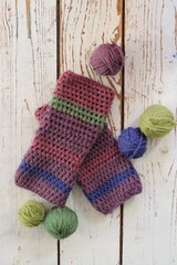 Handmade crochet  striped  mittens  with balls of yarn on a wooden white floor.