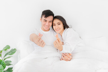 close up hands, Asian lover show heart sign with hands, they rest on white bed, they feeling happy and smiling, happiness honeymoon and valentine's day