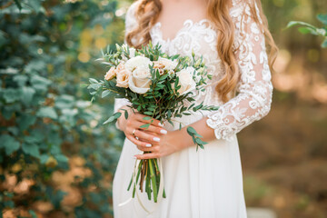 Beautiful wedding bouquet in hands of the bride. Rose, pink and Peach. Trendy and modern wedding flowers. Woman in wedding dress outdoors