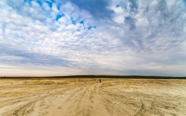 Fototapeta na wymiar Sandy plain and a man in the background against the background of the forest and the blue sky with clouds