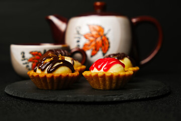 Selective focus homemade chocolate gold and strawberry topping cheese tart on slate plate with coffee cup and pot insight.