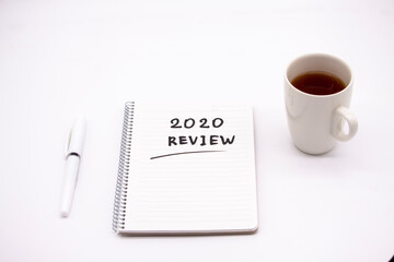 Notepad inscribed 2020 review with pen and tea cup on a white background