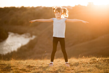 Little girl doing fitness exercises outdoor at sunset