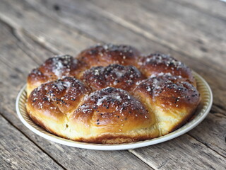 Homemade cake.Buns filled with jam, sprinkled with sesame seeds and icing sugar on a porcelain plate on an ancient wooden table.