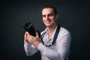 Photographer on a gray background. A man in a white shirt holds a camera in his hands. Studio portrait