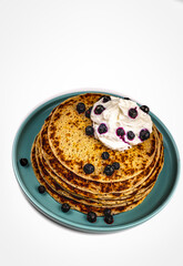 A stack of pancakes on teal plate with blueberries