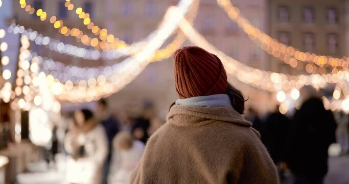 Woman enjoying winter holidays at Christmas market, walking New Year's decorated city in the evening. Handheld video shot