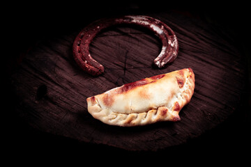 empanada criolla y herradura de caballo oxidada sobre tronco de arbol