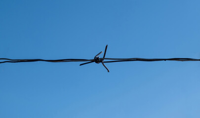 Horizontal sharp wire barb isolated on blue sky background. Closeup.