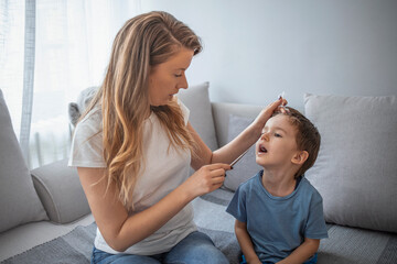 Small boy having a rapid COVID-19 test at home during coronavirus pandemic. Mother using cotton swab while rapid COVID-19 testing small son at home.