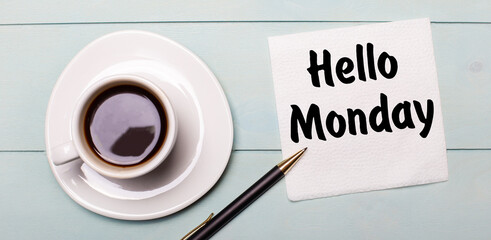 On a light blue wooden tray, there is a white cup of coffee, a handle and a napkin that says HELLO MONDAY.