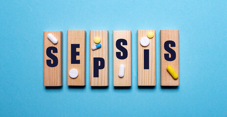 The word SEPSIS is written on wooden blocks on a blue background near the pills. Medical concept