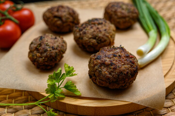 Homemade fried meatballs, served on wooden cutting board with tomatoes, onions and parsley