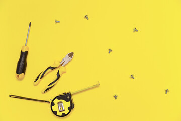 A flatlay with a set of bench tools, screwdriver, cutting pliers, tape measure and screws on yellow Illuminating background. Colors of the 2021 year.