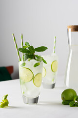 Refreshing cold drinks with lime and mint, glasses with lemonade and ice and straws, jug with drink on white background