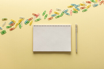 Open spiral notepad on yellow background , notebook and pen lie on textural paper, flat lay concept in trendy colors of the year, paper clips of different colors