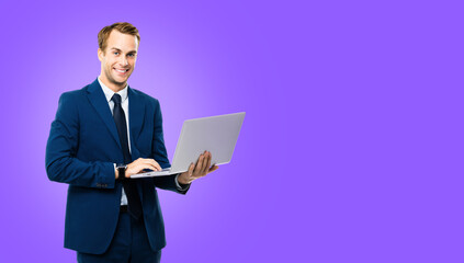 Smiling businessman in blue confident suit, working with laptop, over violet purple color background. Handsome young man at studio concept picture. Copy space.