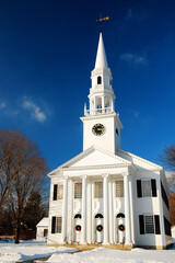 A white steeple church stands in a yard covered in snow