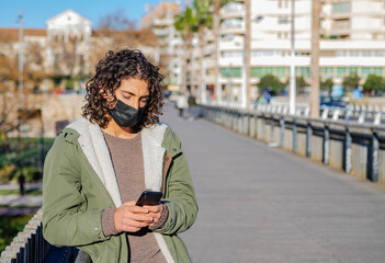Young Caucasian male wearing a mask and checking his phone on a street - Powered by Adobe