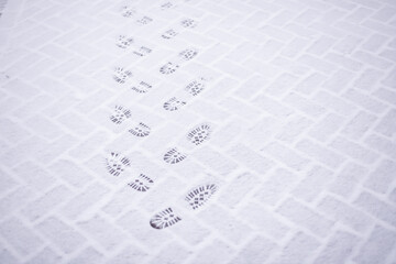 Footprints on first fresh white snow on asphalt.