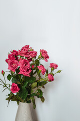 Pink roses in a vase on a white background. The concept of the coming of spring and women's day. Minimalistic lifestyle background.