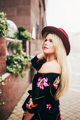 Spectacular middle-aged blonde woman in hat and dress walks through the streets of the old city