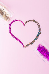 Heart shape made of multicolored glitter. Two champagne glasses with splash of heart shaped confetti over pink background. Valentine's Day concept. Flat lay
