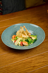 Caesar salad with shrimp on blue plate on wooden background