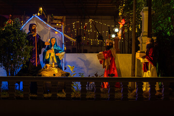 Outdoor Christmas Crib scene decorated with lights. Holy family. Nativity scene using handmade manger and figurines. Decorations in the period of advent