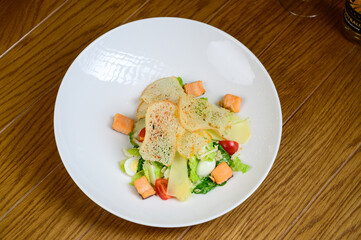Caesar salad with salmon on white plate on wooden background