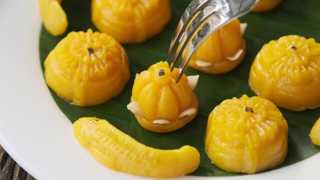 Fork is dipping into the dessert Thong-Eek, Sane Chan and Kanom Jamongkut (Thai sweets) on a white plate with banana leaves.