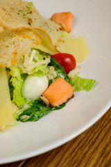 Caesar salad with salmon on white plate on wooden background